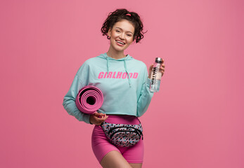 Wall Mural - smiling happy beautiful woman in stylish sports outfit posing on pink background isolated in studio