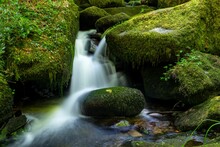 Natural Landscape View Of A Small Stream Flowing Through Mossy Rocks
