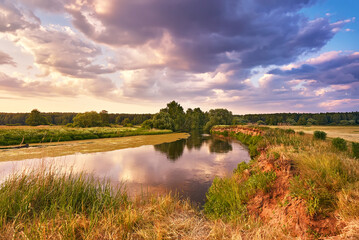 Wall Mural - Landscape with sunset over river. Evening with Dramatic beautiful clouds on sky. Water reflection. Trees on riverbank. Weather change. Green filed and meadow.