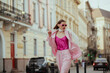 Fashionable elegant confident woman wearing trendy pink sunglasses, suit blazer, satin top, white silk scarf, trousers, walking in street of European city. Copy, empty space for text