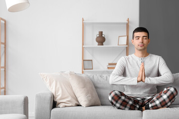 Canvas Print - Young man in pajamas meditating on sofa at home