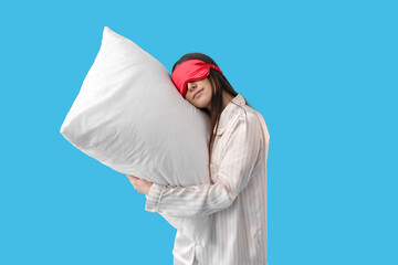 Wall Mural - Young woman with sleeping mask and soft pillow on blue background