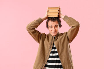 Wall Mural - Young man with stack of books on pink background