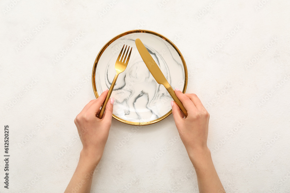 Female hands with cutlery and empty plate on white table
