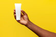 © Богдан Маліцький - hand of african american man holds and offers white tube of cosmetic cream on yellow isolated background