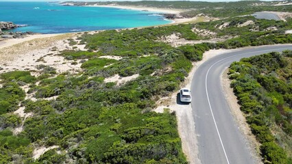 Wall Mural - Drone footage over cars on highway by turquoise sea water with green hills in the summer