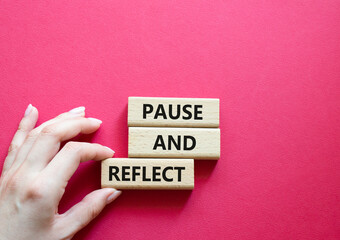 Pause and Reflect symbol. Concept words Pause and Reflect on wooden blocks. Beautiful red background. Businessman hand. Business and Pause and Reflect concept. Copy space.