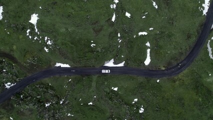 Sticker - Top view aerial footage of green highlands partially covered in snow and a car driving on a road