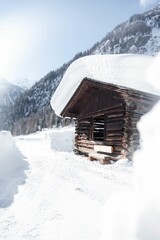 Canvas Print - Vertical shot of a wooden house covered in snow with mountains in the background on a sunny day