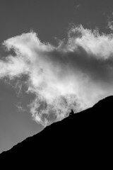 Wall Mural - Vertical grayscale of a person sitting on the slope of a mountain against a dramatic sky