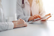 © rogerphoto - Doctor and patient sitting at the desk in clinic office. The focus is on female physician's hands using tablet computer, close up. Perfect medical service and medicine concept.