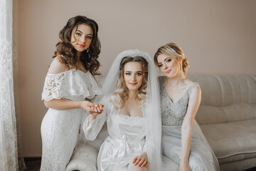 The bridesmaids are looking at the camera. The bride and her fun friends celebrate the bachelorette party in different dresses. Bride and friends in the room