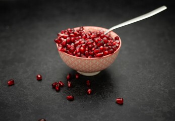 Poster - A bowl of red pomegranate  seeds, served with a spoon, and pomegranate seeds around the bowl