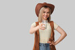 Beautiful cowgirl with glass of milk on grey background