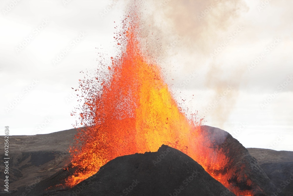 Volcanic eruption with glowing orange lava flow surrounded by a pool of ...