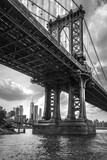 Fototapeta Mosty linowy / wiszący - Brooklyn Bridge over The East River in New York, with a cityscape in the background, in a grayscale