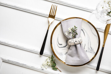 Plate with folded napkin, gold cutlery and glass on wooden white background