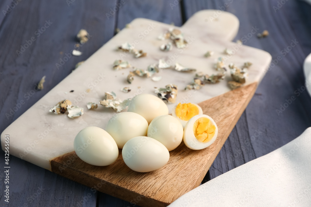 Board of boiled quail eggs and shells on blue wooden background