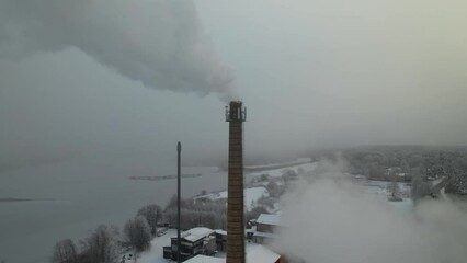 Sticker - Drone shot over snowy houses with long chimneys with smoke in the misty sky in the winter