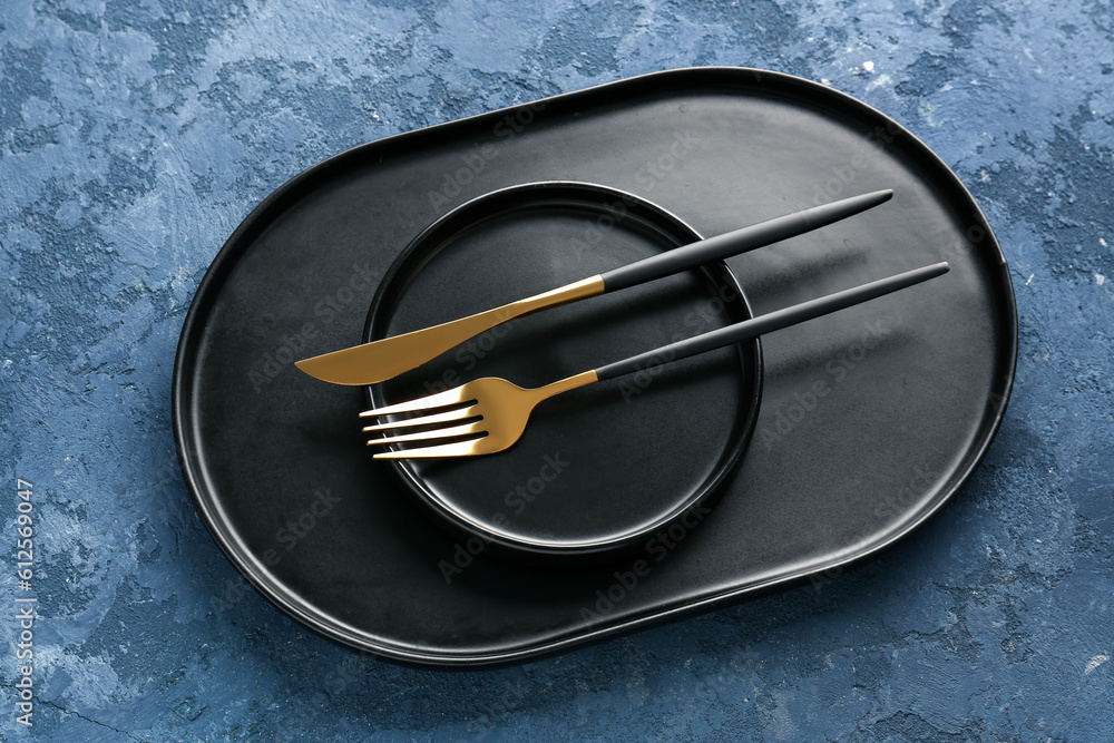 Golden fork with knife, black plate and tray on blue grunge background