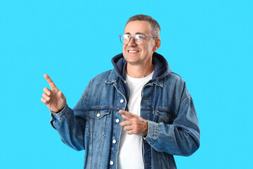 Wall Mural - Mature man in eyeglasses pointing at something on blue background