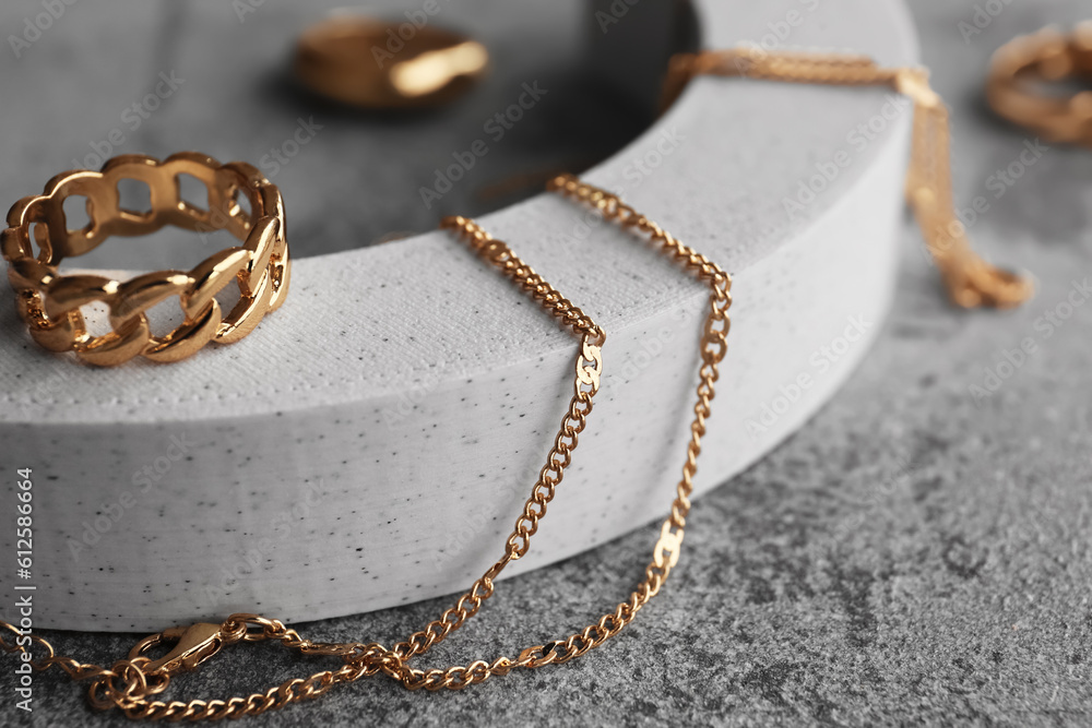Decorative podium with different golden rings and necklaces on grunge grey background