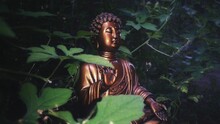 Brown Buddha Statue In Meditation In The Forest With Green Plants Around