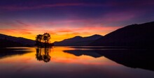 Scenic Sunset Over A Lake With The Reflection Of Trees And Hills On Its Surface
