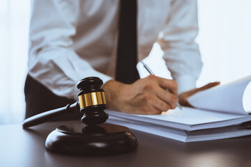 Wall Mural - Focus wooden gavel hammer on blur background of lawyer working with legal document on desk at law firm office. Lawful hammer for righteous and equality judgment by lawmaker and attorney. Equilibrium