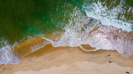 Drone shot of the sandy shore of a lake with green water on a sunny day