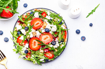 Wall Mural - Strawberry salad with arugula, lettuce, blueberries, feta cheese and walnuts, white table. Fresh useful dish for healthy eating