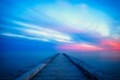 Long wooden pier extends out into a tranquil body of water during the pink and blue sunset