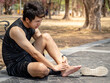 Asian athlete man touching foot in pain due to sprained ankle while running in the park. Broken twisted ankle sprain or foot cramp. Sport injury concept
