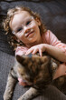 © Serena Burroughs/Stocksy - Girl petting her cat while sitting on couch