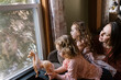© Serena Burroughs/Stocksy - Mother and her daughters looking out of the window together