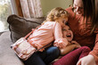 © Serena Burroughs/Stocksy - Happy mother and daughters sitting on couch, laughing together