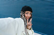 © Ezequiel Giménez/Stocksy - Stylish woman showing victory sign against blue wall