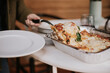 © Jarusha Brown/Stocksy - Woman serves a portion cooked lasagna from a tray.