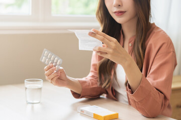 Health care treatment asian young woman holding prescription of capsule medicine, reading label text about medical information, looking medicine instruction side effects, pharmacy medicament concept.