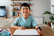 © Santi Nuñez/Stocksy - Boy smiling while doing homework at home.