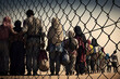 canvas print picture - Eine Gruppe von Flüchtlingen steht vor einem Zaun an der Grenze