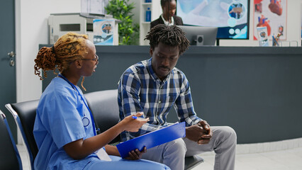 Wall Mural - Medical assistant explaining diagnosis to sick man, showing checkup report papers in hospital waiting area. Young patient talking to nurse about disease and treatment, doing consultation.