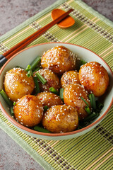 Sticker - Glazed potatoes served with green onions and sesame seeds close-up in a bowl on the table. Vertical