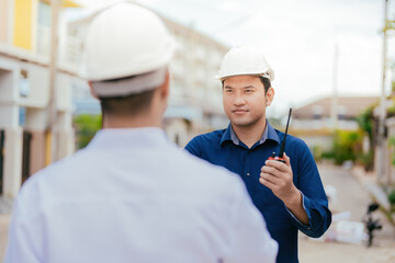 Wall Mural - Shoulder-to-shoulder photograph between two Asian male engineers as a manager Talking about design work in the design of construction work in the architectural industry holding a radio wear a helmet