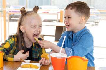 Happy little children brother and sister eating french fries at fast food restaurant. Unhealthy meal for kids. Junk food. Overweight problem child.