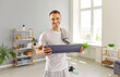 © Studio Romantic - Portrait of a happy man with a towel on his shoulder holding a yoga mat, looking at camera and smiling. Sport, workout, fitness exercise, wellness, physical activity at home concept