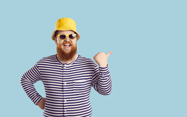 Studio portrait of funny fat ginger man in swimwear, hat and sun glasses enjoying summer holidays, smiling and pointing at blank empty copyspace background on right side. Sale, fun, pool party concept