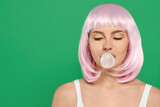 Fototapeta Sypialnia - Beautiful woman blowing bubble gum on green background, space for text