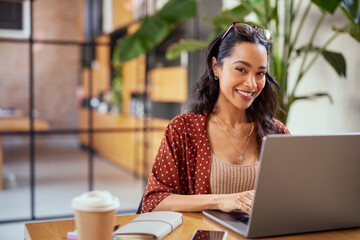 Smiling woman working on laptop and looking at camera