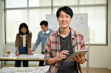 Wall Mural - A smart Asian male website developer stands in the office with a digital tablet in his hand